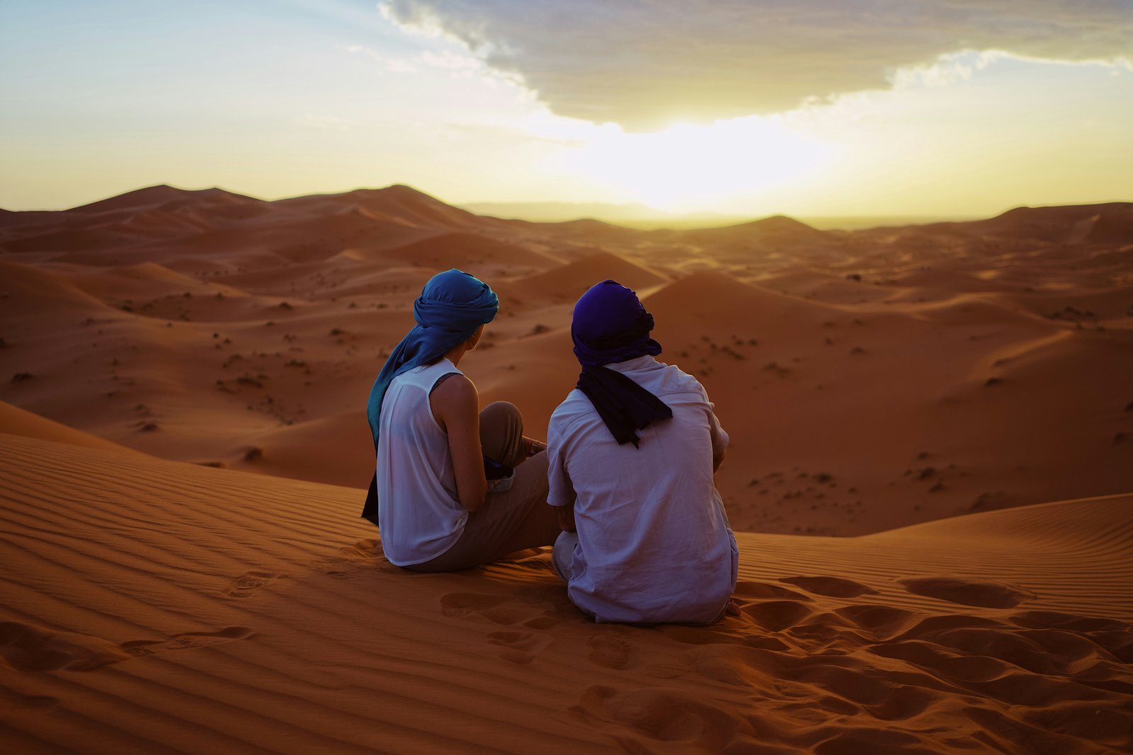 Morocco honeymoon — couples sitting in the Sahara desert wearing traditional Moroccan scarves, Merzouga